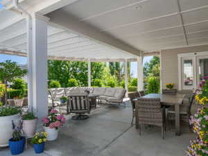 Expansive covered patio featuring a slatted pergola extension, recessed lighting, concrete flooring, and direct access to the interior via double glass doors