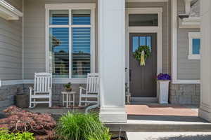 Inviting front porch featuring a dark entry door with window panes, light gray siding, and a stone veneer foundation