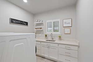 Laundry room featuring white cabinetry, a light-colored countertop, and a stainless steel sink with a gooseneck faucet