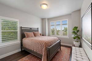 Spacious bedroom featuring multiple windows with louvered shutters, dark wood-finish flooring, and a ceiling-mounted light fixture