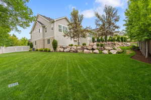 Expansive backyard featuring a manicured lawn, established trees, and a terraced rock garden