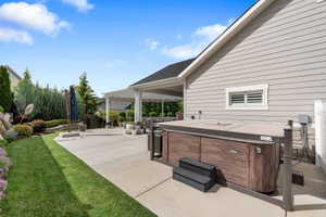 Private backyard featuring a built-in hot tub with dark wood-finish paneling, a spacious concrete patio, a manicured lawn, an extensive terraced garden with mature shrubs and flowering plants, and a covered pergola