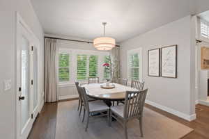 Dining space featuring dark wood-finish flooring, white plantation shutters, and a contemporary drum pendant light fixture