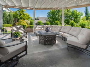 Concrete patio featuring a slatted pergola, decorative patio floor, and terraced landscaping with mature greenery