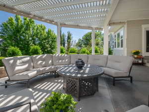 Covered patio featuring a white pergola, concrete flooring, and a light-colored exterior wall with a white trim window