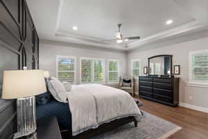 Primary bedroom with Tray ceiling and recessed lighting and a ceiling fan, plank wood-finish flooring, and multiple windows with plantation shutters