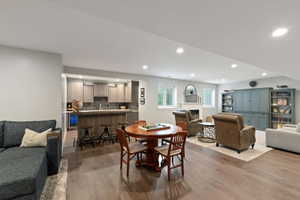 Lower level entertainment space featuring wood-finish flooring, a wet bar with cabinetry and integrated beverage cooler, a built-in media center, and a fireplace with a white mantel and surround
