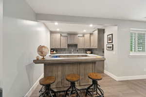 Custom bar featuring a light wood-finish base, stone countertop, and recessed lighting