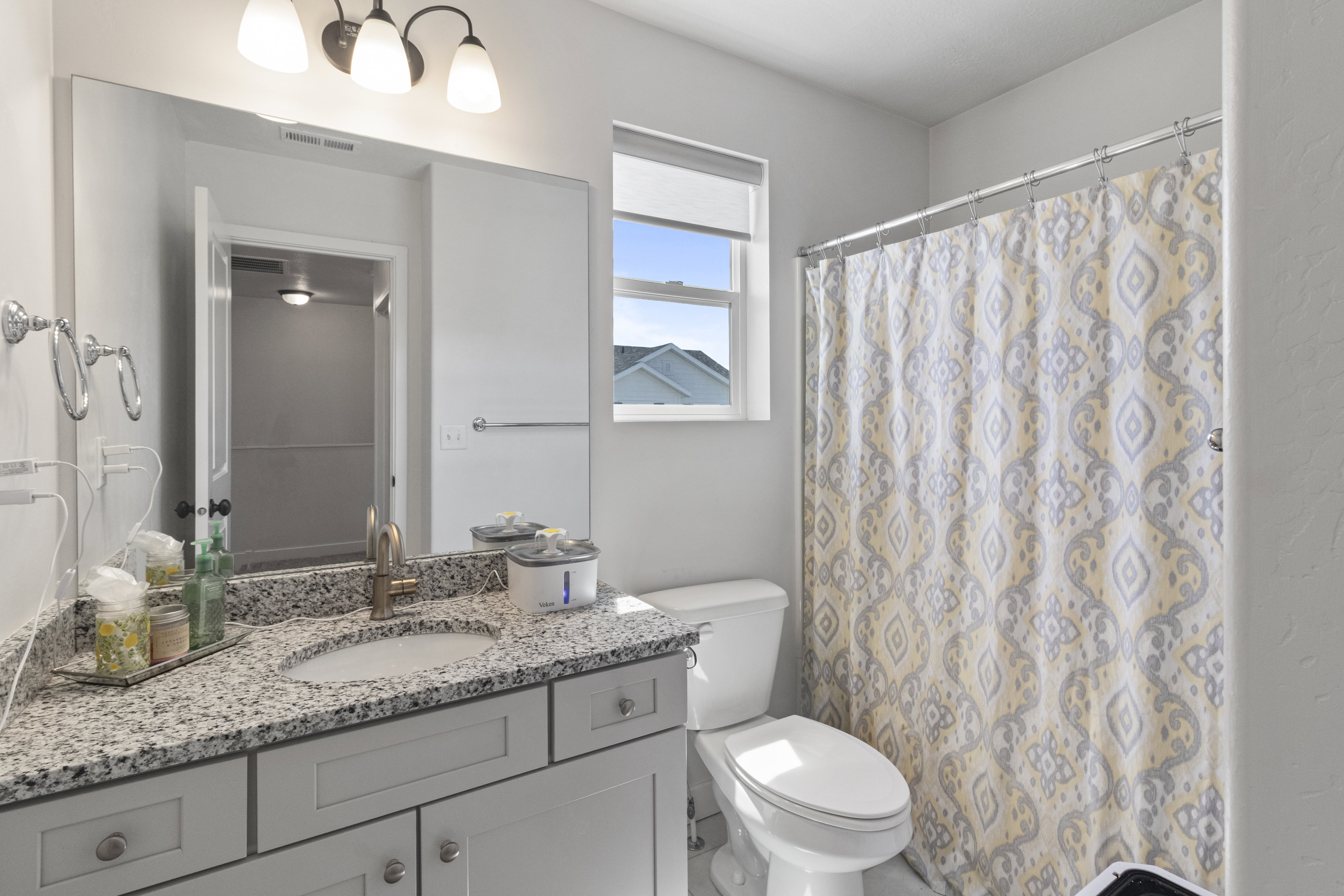 Bathroom featuring a light-toned granite countertop with an undermount sink, a vanity with paneled cabinetry, and a mirrored wall