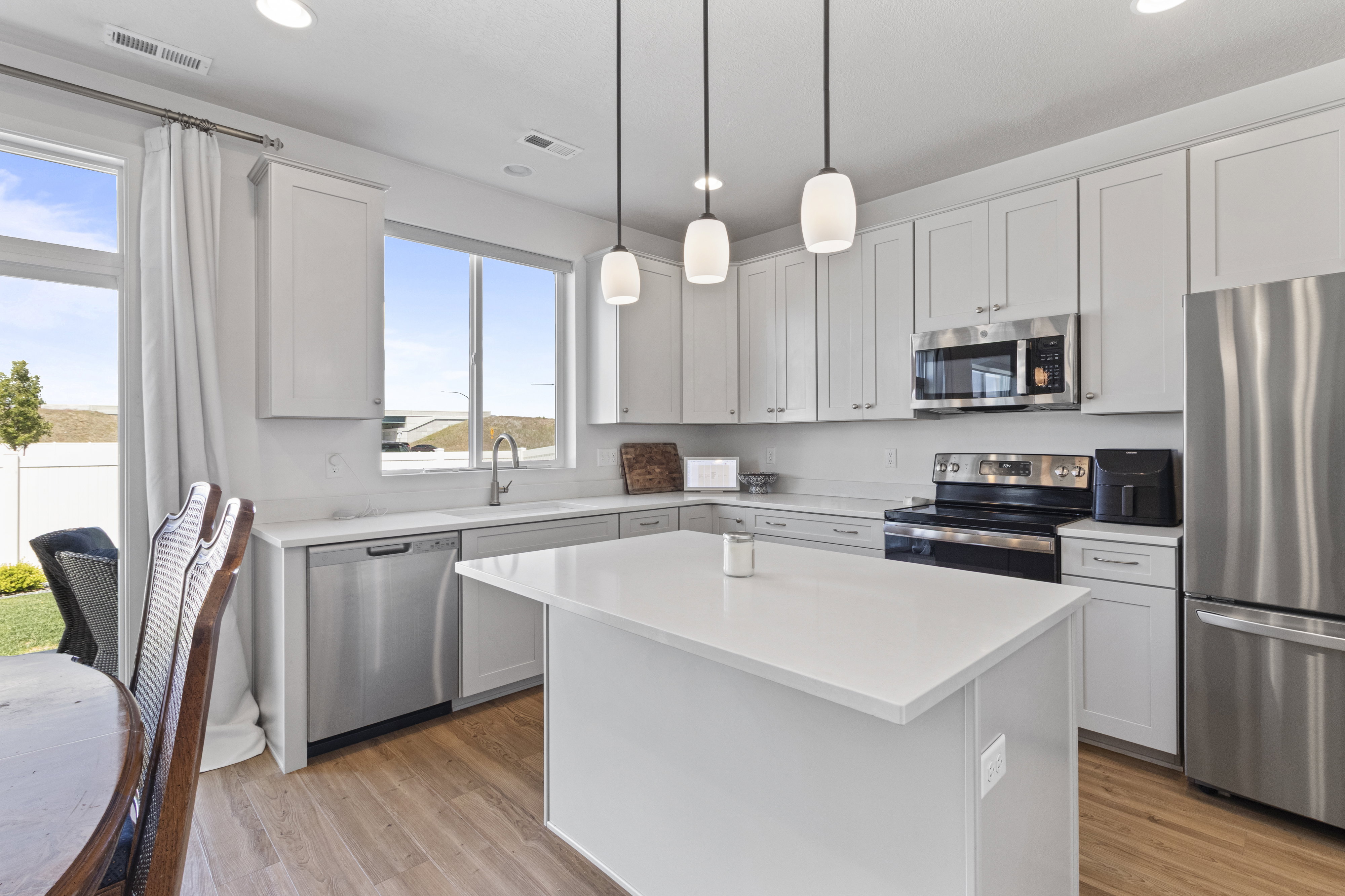 Modern kitchen featuring white shaker cabinetry, stainless steel appliances, a center island with a solid surface countertop, LVP flooring, and pendant lighting