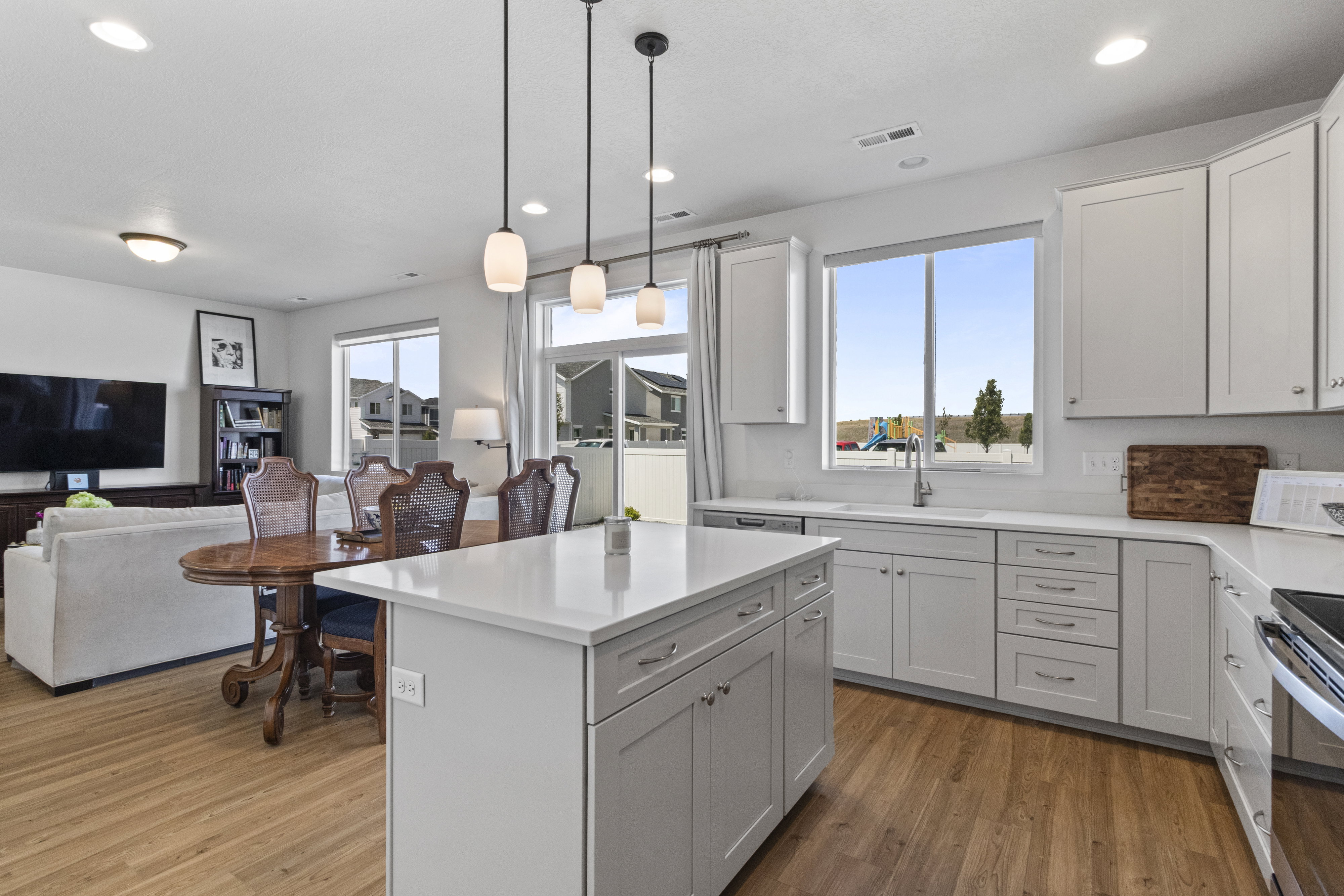 Open-concept kitchen featuring an island with a light-toned countertop, white cabinetry, a built-in sink with a window, LVP flooring, and pendant lighting