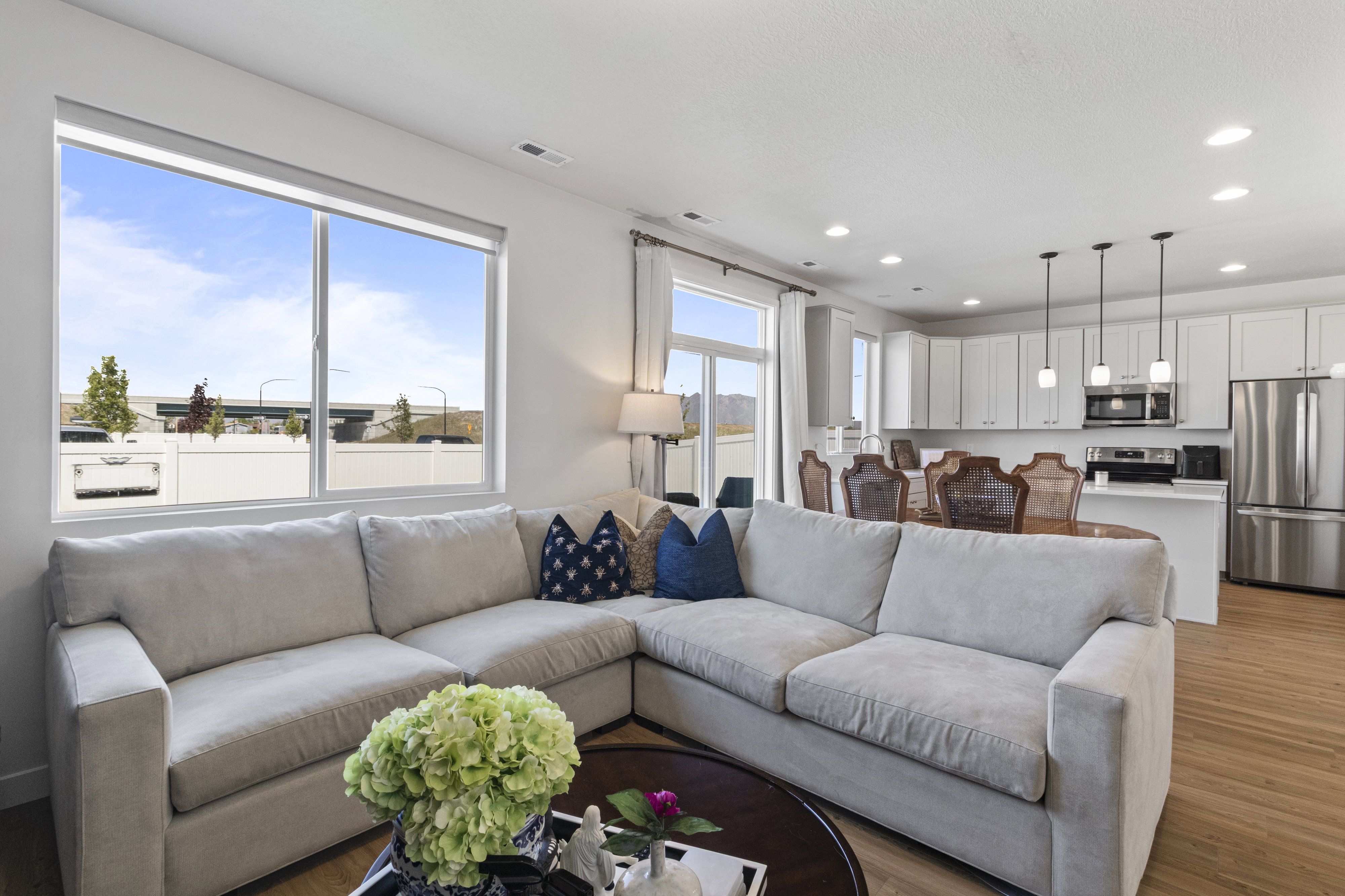 Open-concept living area featuring a large window, light wood-finish flooring, recessed lighting, white cabinetry, and stainless steel appliances