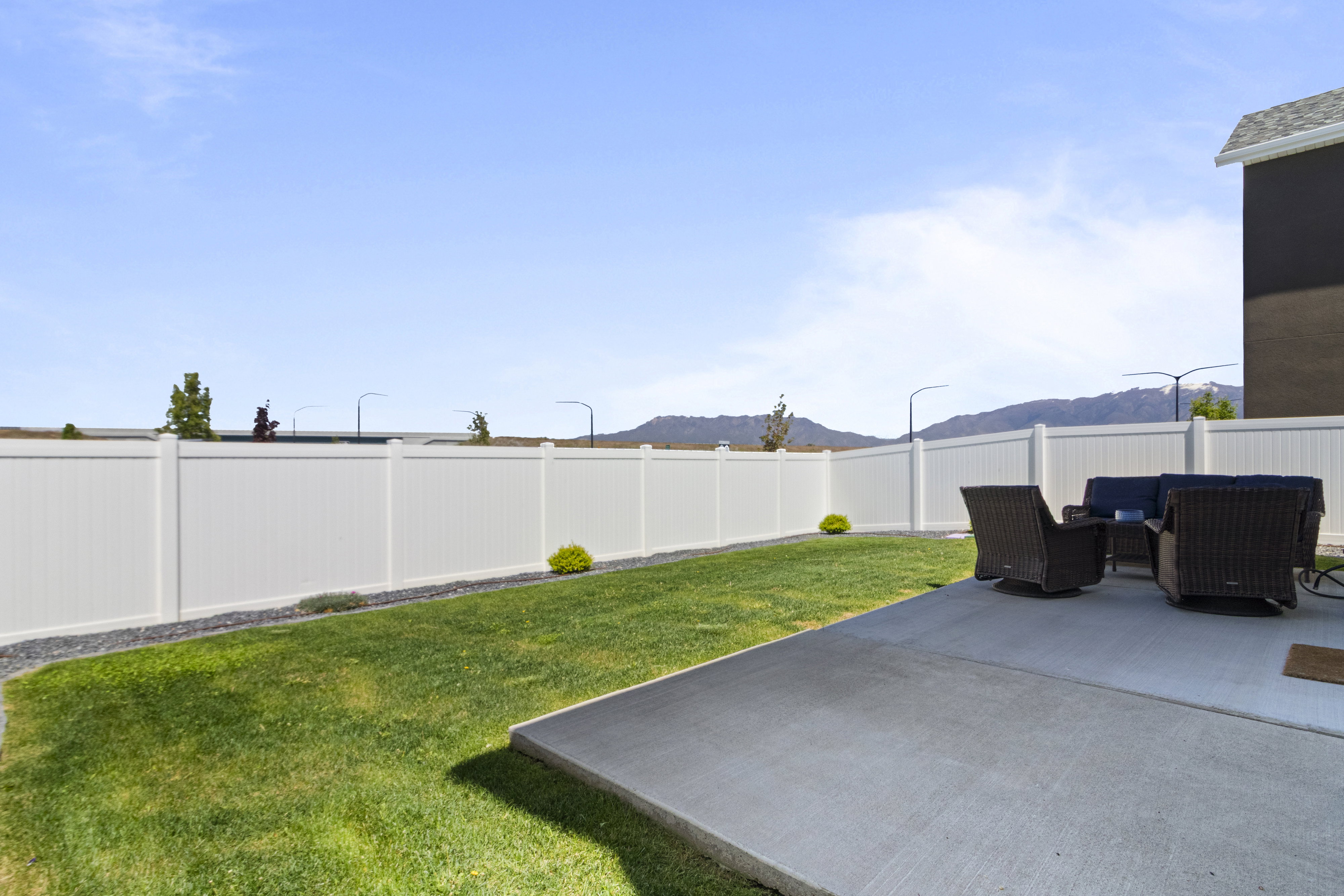 Backyard featuring a lush lawn, concrete patio, and white privacy fencing