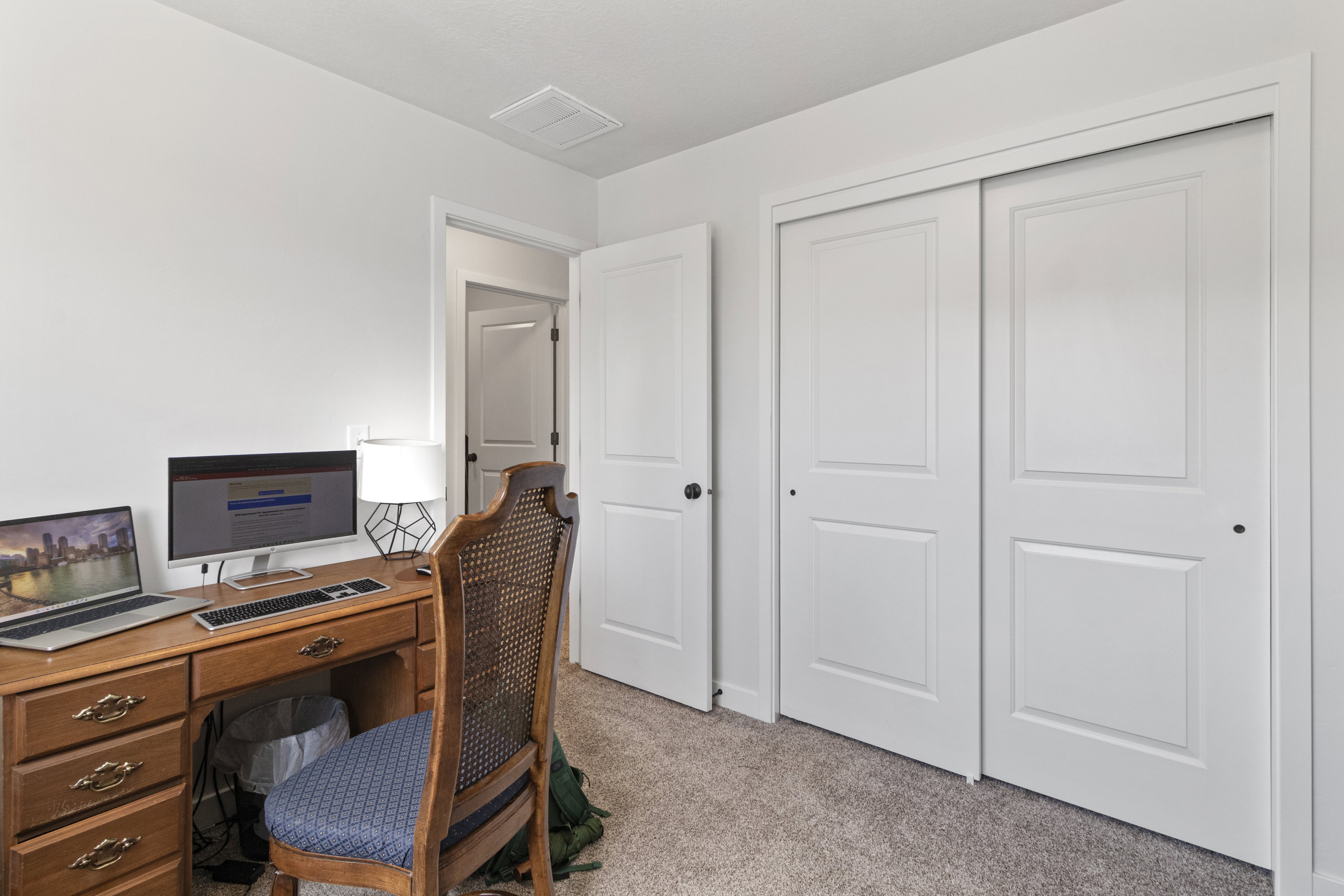 Neutral tone wall paint, light-colored carpet flooring, white paneled doors, and a white ceiling with a visible vent