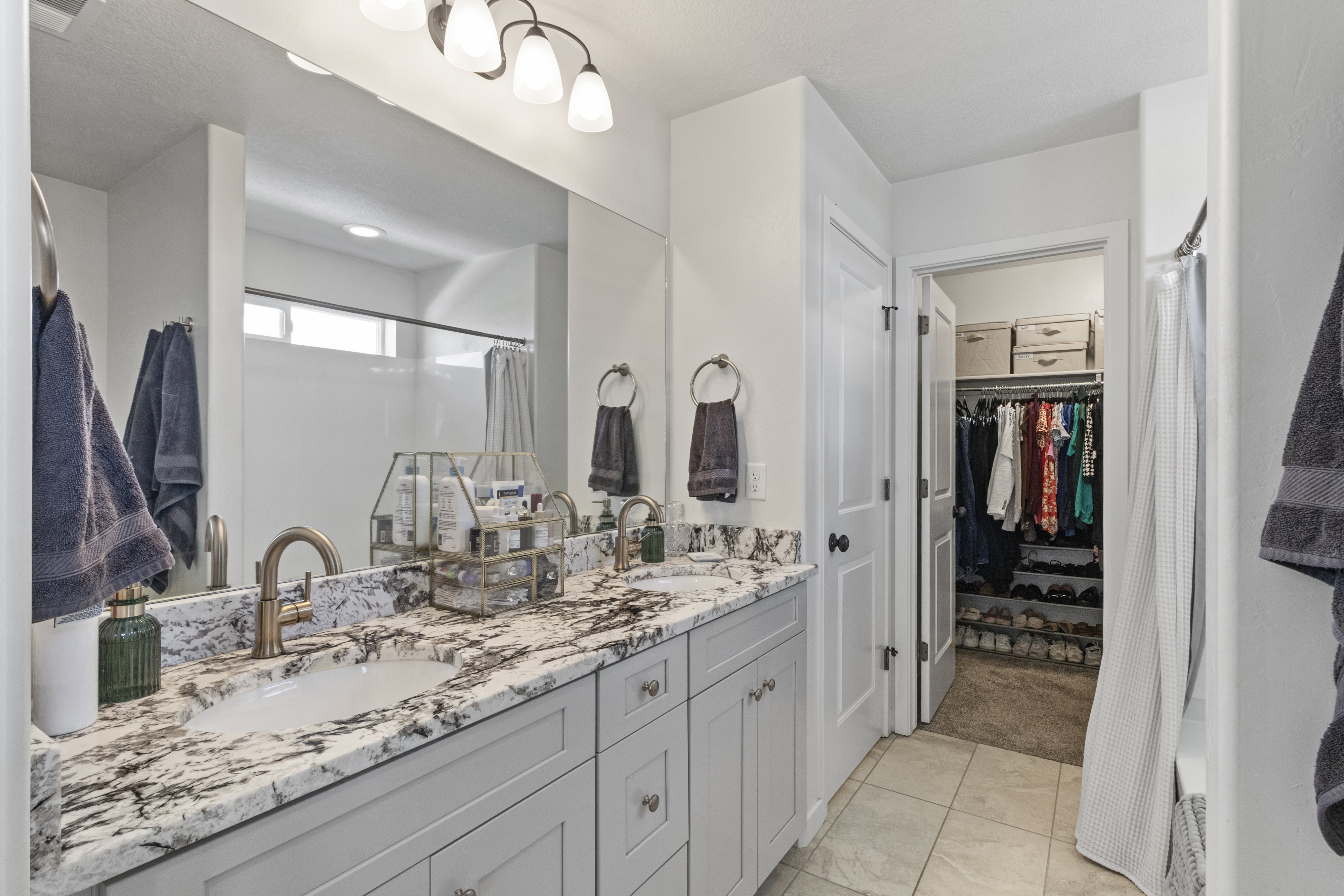 Double vanity featuring light gray cabinetry, bronze-finish fixtures, and a natural stone countertop