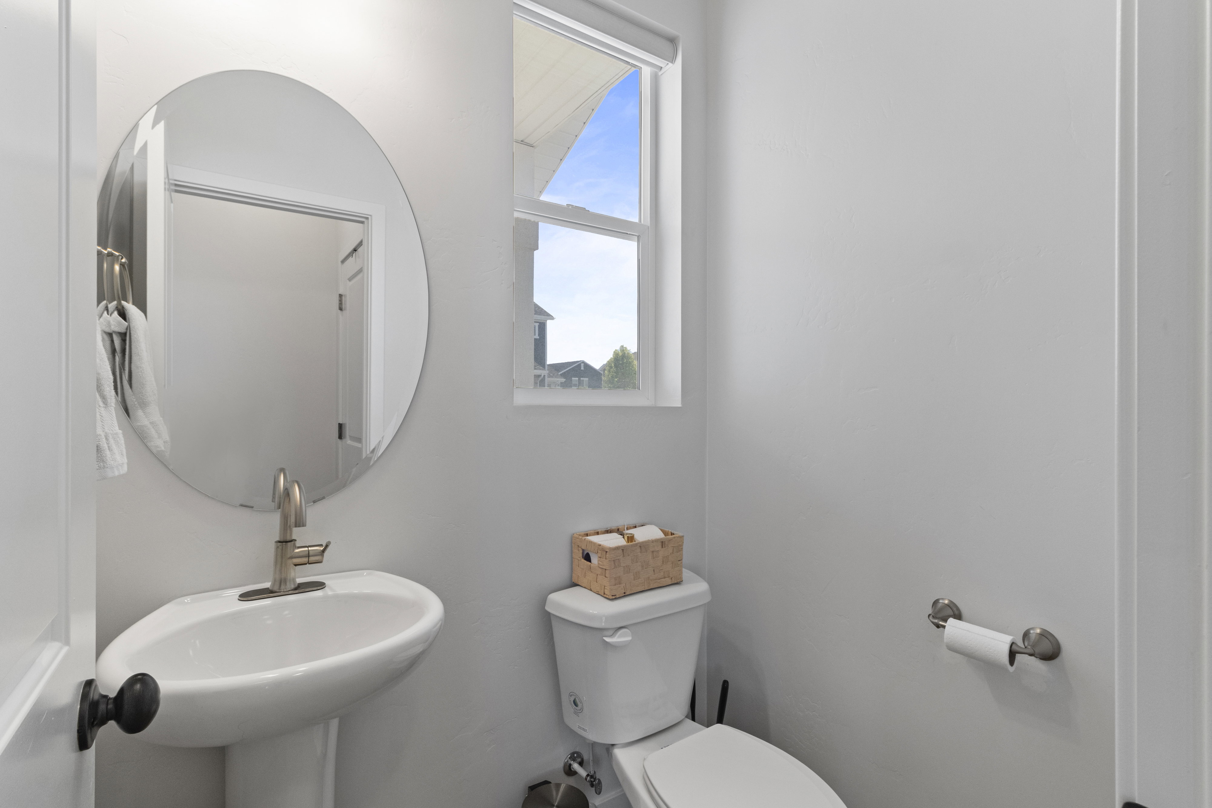 Pedestal sink with brushed nickel faucet, round wall-mounted mirror, and white toilet