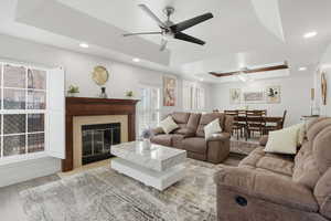 Spacious living area featuring a fireplace with a wood mantle, wood-finish flooring, recessed lighting, and a tray ceiling with a ceiling fan