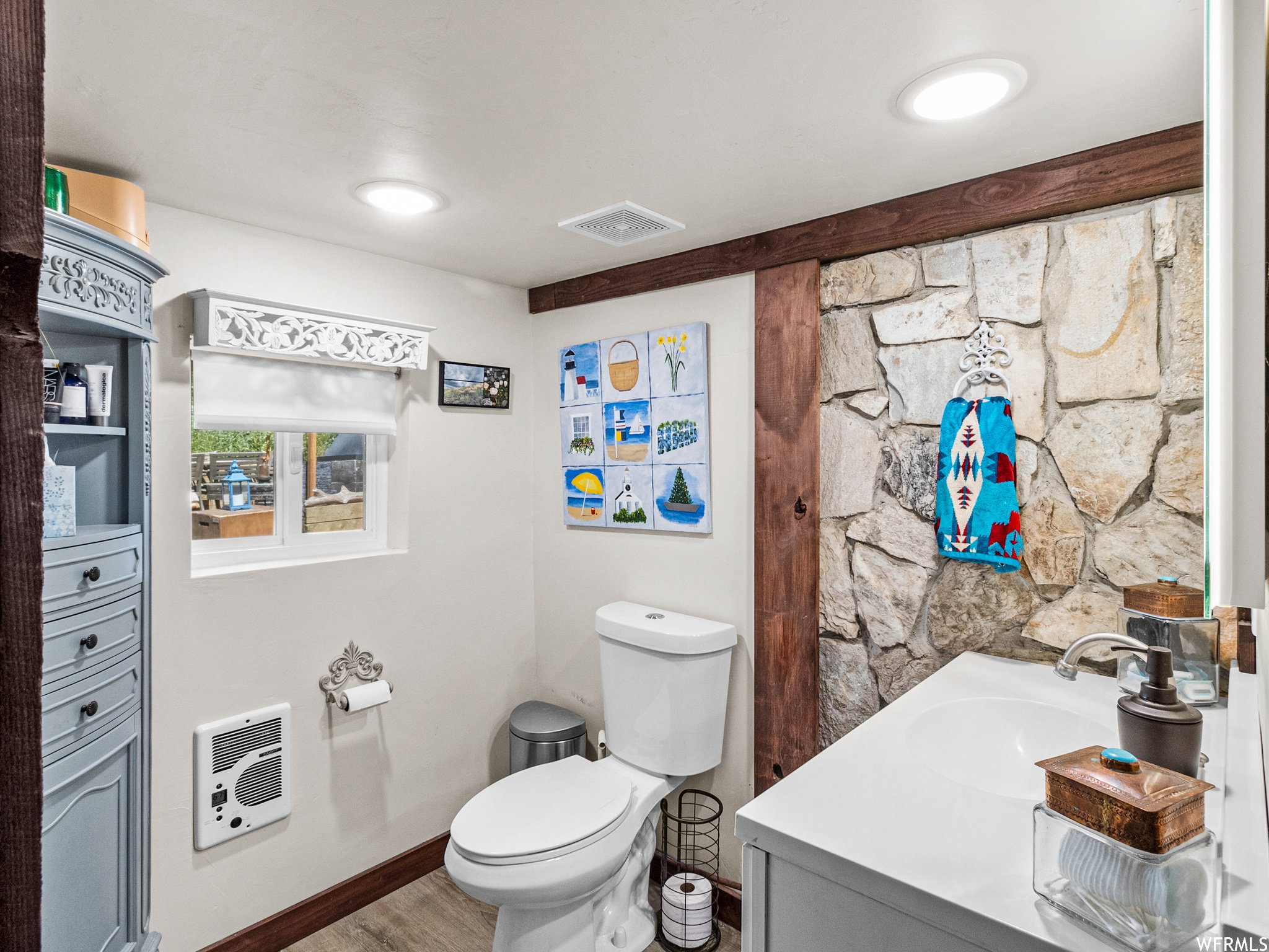 Bathroom featuring a stone accent wall, wood-finish flooring, white vanity with integrated sink, and recessed ceiling lighting