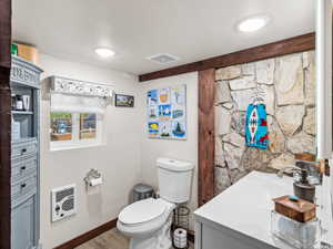 Bathroom featuring a stone accent wall, wood-finish flooring, white vanity with integrated sink, and recessed ceiling lighting