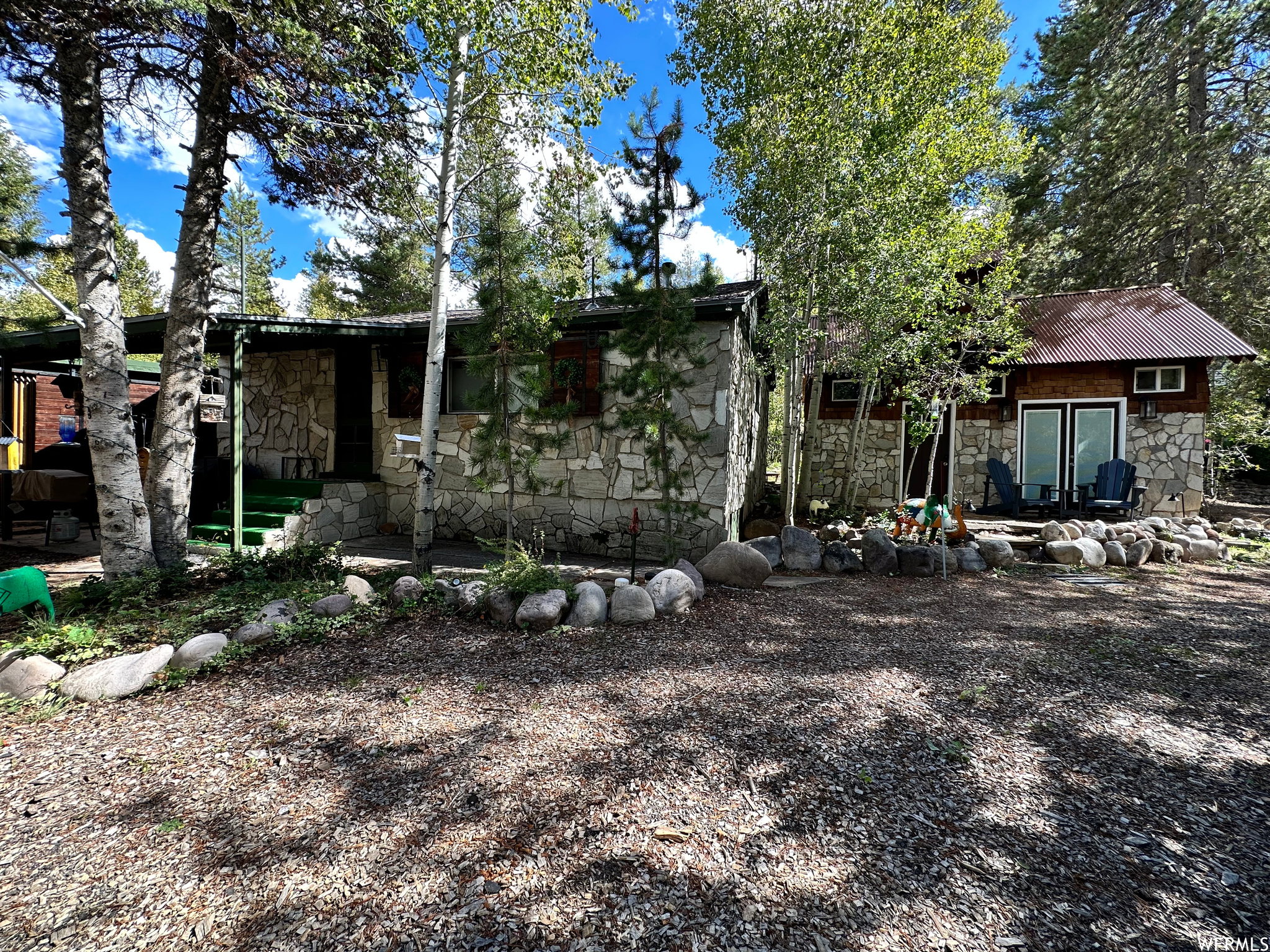 Stone-sided cabin featuring a covered entry and a separate stone-sided guest house with a metal roof and double patio doors