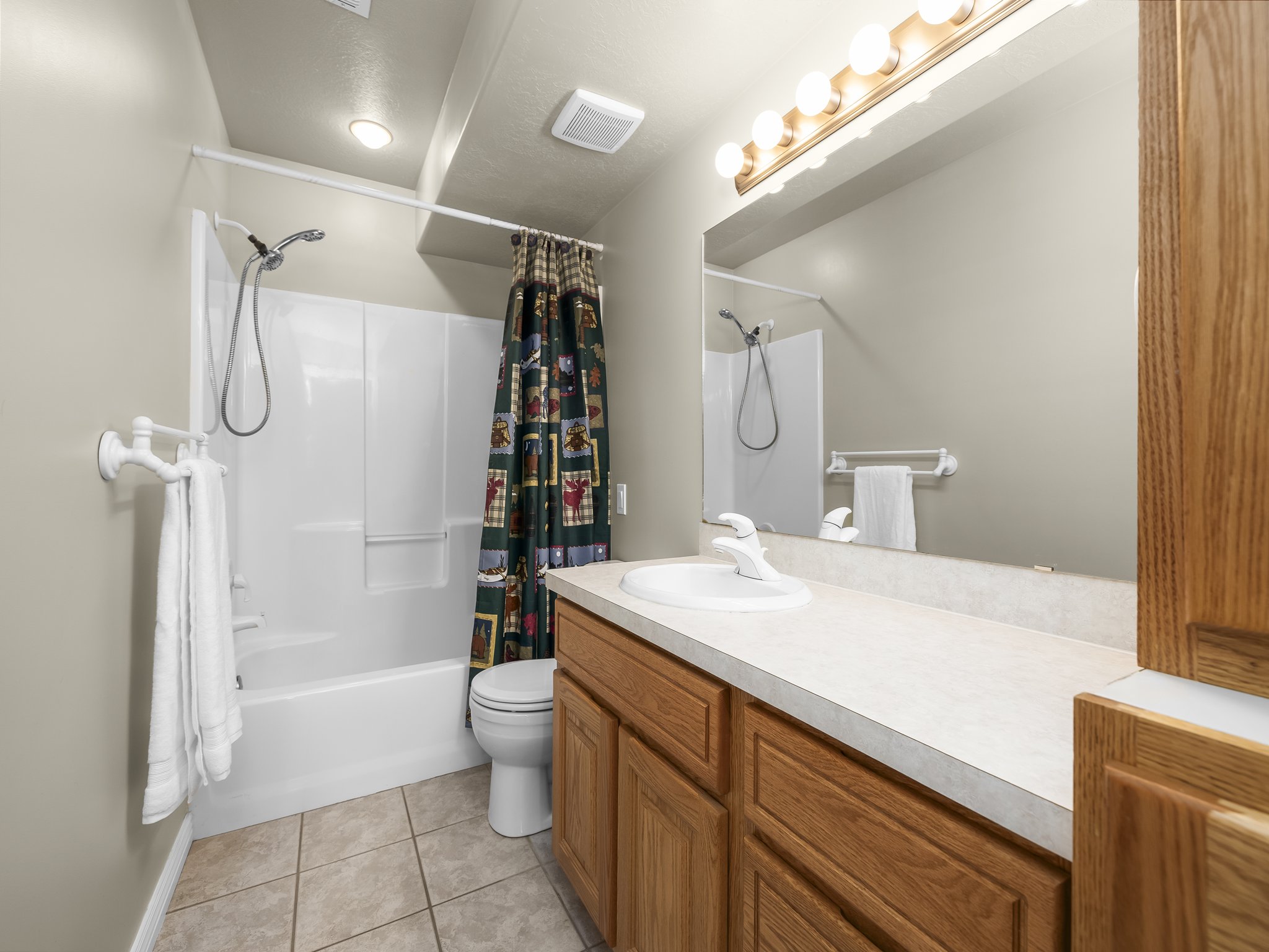 Bathroom featuring a white tub-shower combination with a handheld shower head, a light wood-finish vanity with a built-in sink, a large wall-mounted mirror, and tile flooring