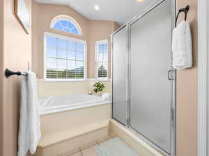 Bathroom featuring a built-in soaking tub with tiled surround, an arched accent window, and a separate shower with frosted glass doors