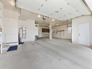 Spacious garage with light-toned concrete flooring, overhead lighting, windows, built-in cabinetry, and a service door