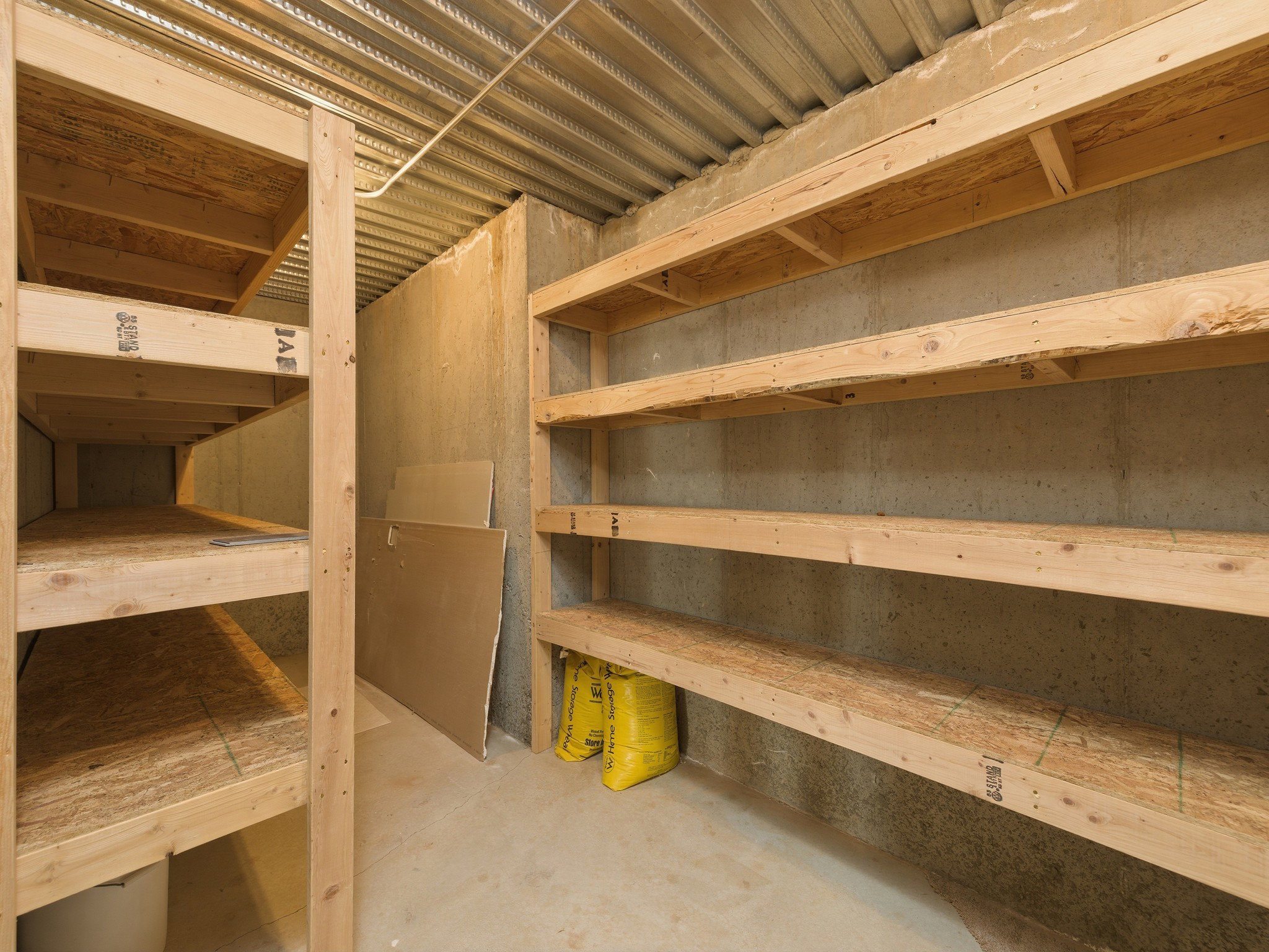 Extensive built-in shelving units in a concrete-walled space, featuring wood-finish shelving and a corrugated metal ceiling