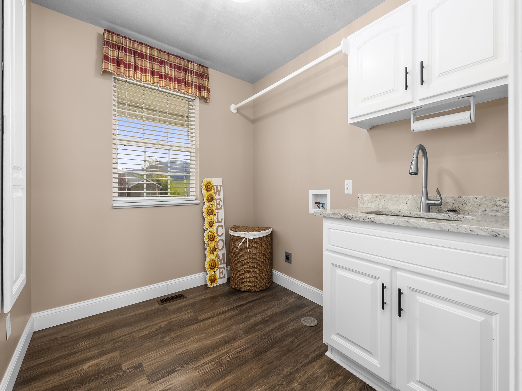 Utility area featuring wood-finish flooring, a single window with blinds, white cabinetry, a light-toned countertop, and a stainless steel sink with a gooseneck faucet
