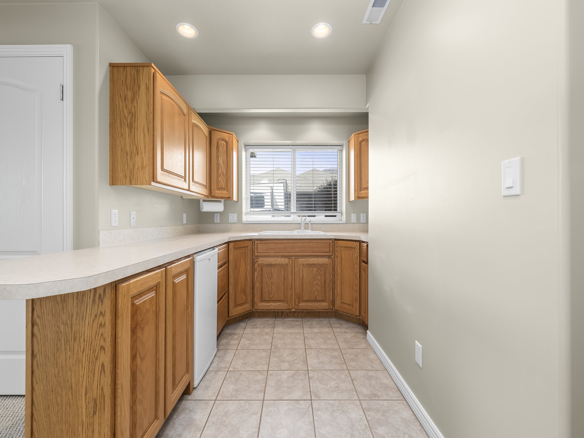 Kitchenette featuring wood cabinetry, laminate countertops, a built-in sink, an under-counter appliance, and recessed lighting