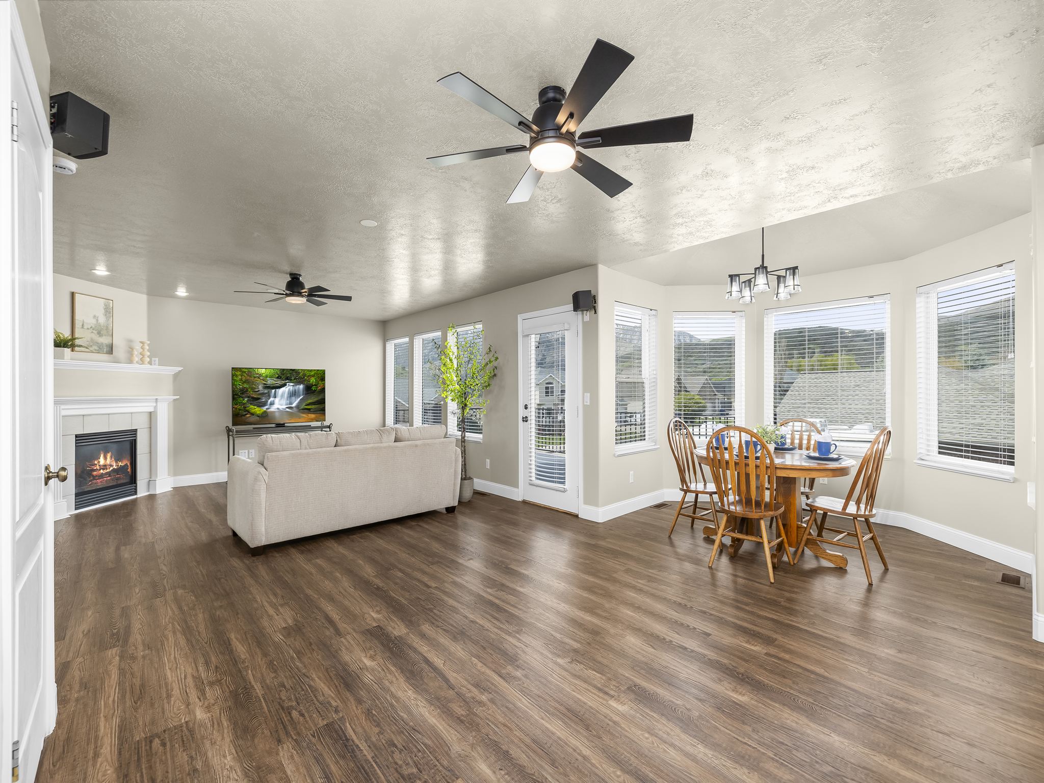 Spacious living area featuring wood-finish flooring, a fireplace with a white mantle, ceiling fans, and a dining nook with bay windows