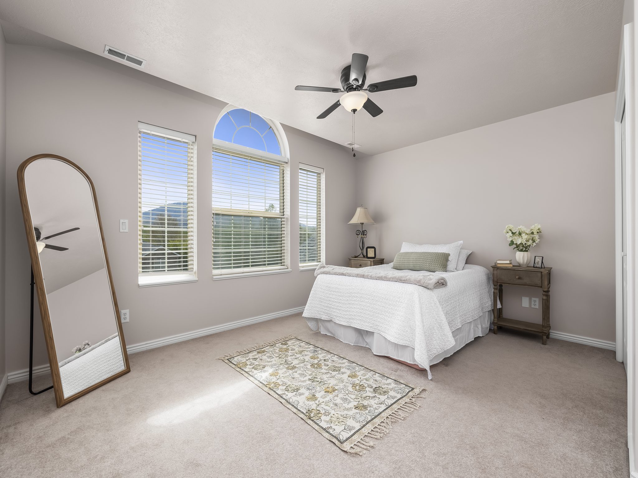 Room featuring three windows with blinds, including an arched transom window, a ceiling fan with integrated lighting, and neutral-toned wall-to-wall carpeting