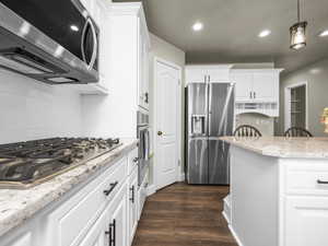 Kitchen featuring white cabinetry, stainless steel appliances, a gas cooktop, stone countertops, and wood-finish flooring