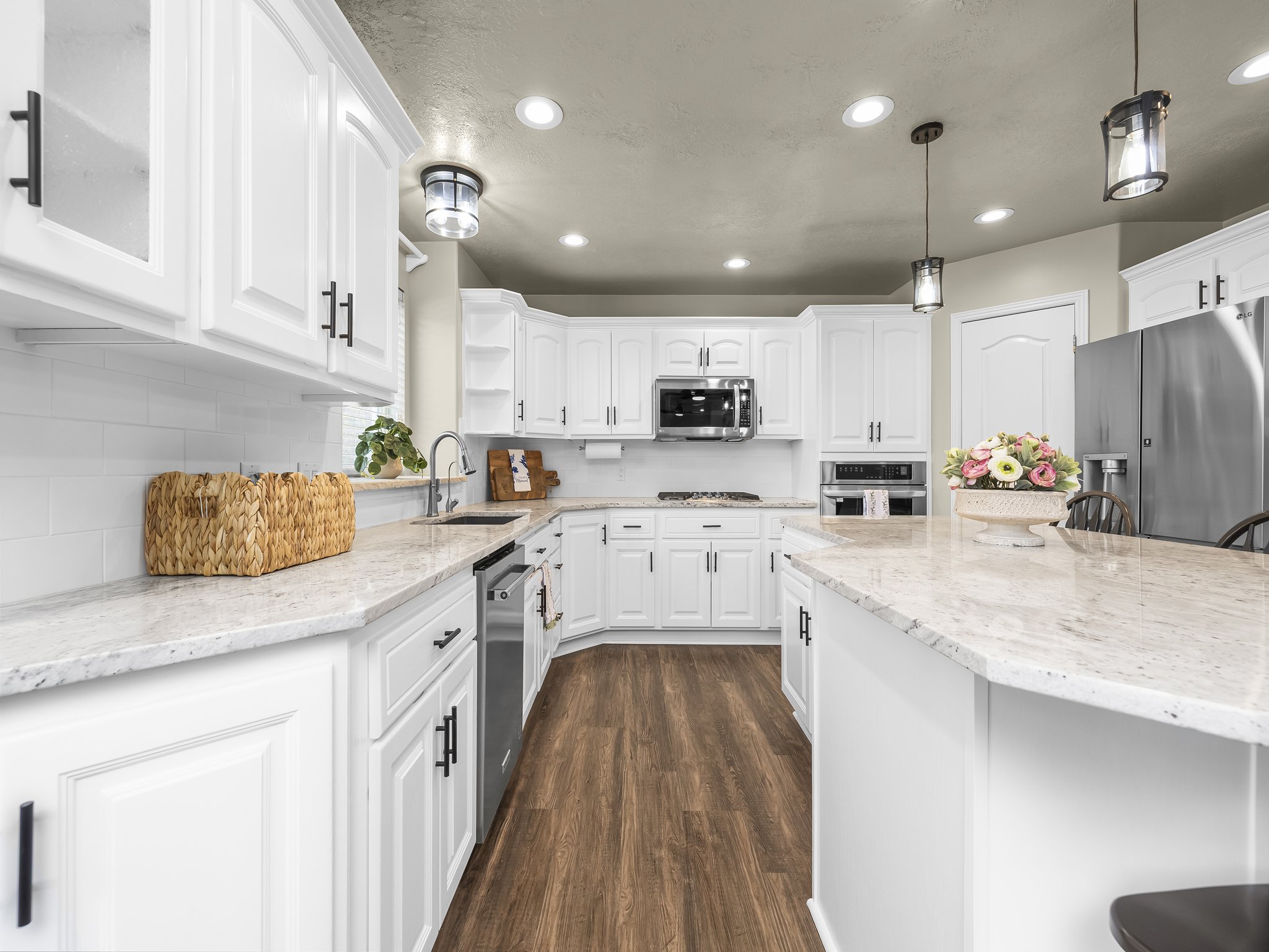 Kitchen featuring white cabinetry with black hardware, light-toned countertops, stainless steel appliances, wood-finish flooring, and pendant lighting