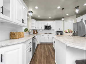 Kitchen featuring white cabinetry with black hardware, light-toned countertops, stainless steel appliances, wood-finish flooring, and pendant lighting