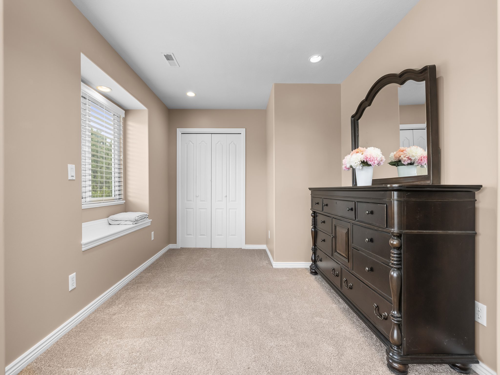 Plush carpeted room featuring a window with built-in bench seating, recessed lighting, and a bi-fold closet