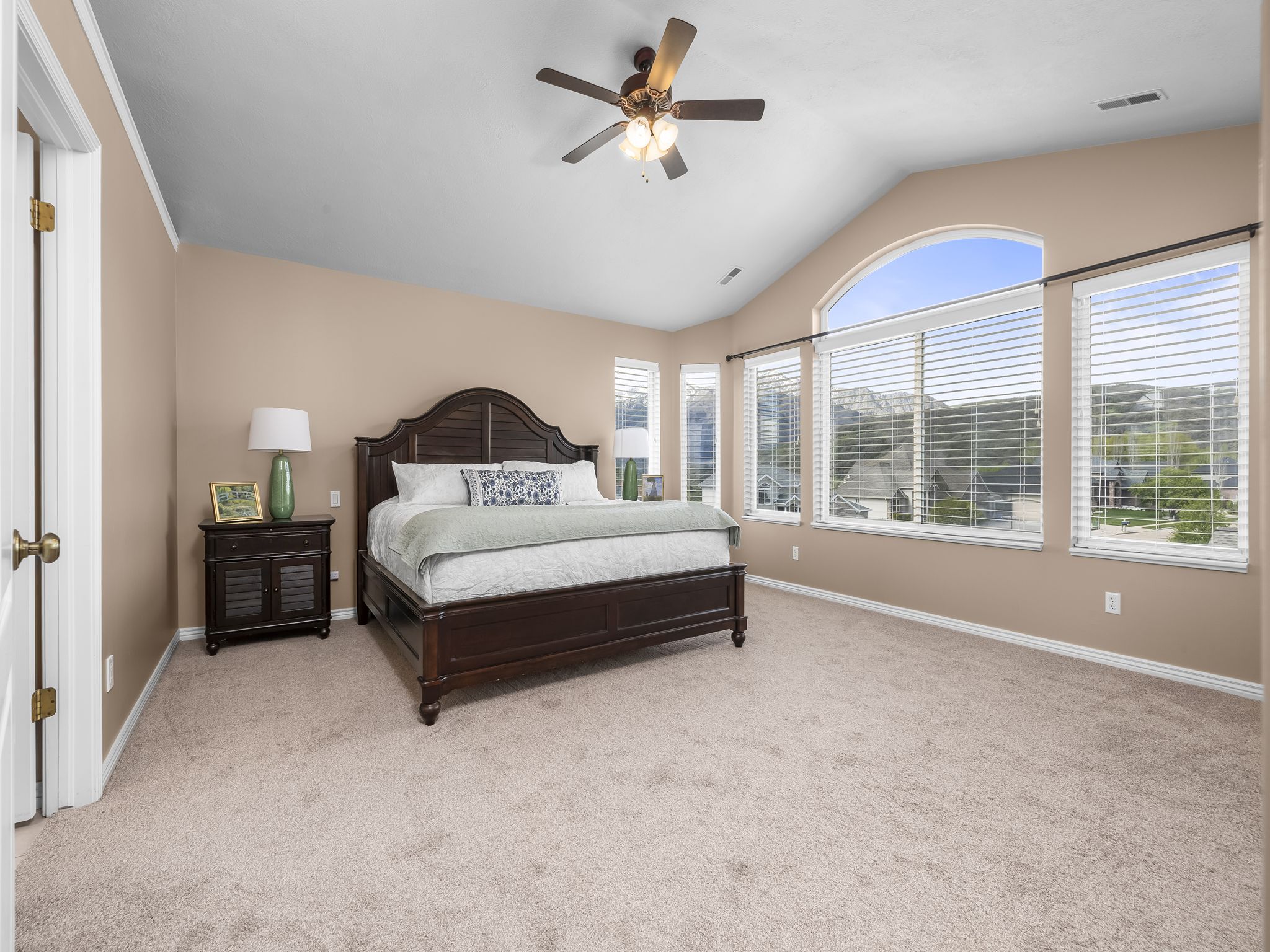 Vaulted ceiling room featuring a large arched window, additional windows with blinds, a ceiling fan, and carpet flooring