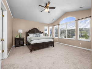 Vaulted ceiling room featuring a large arched window, additional windows with blinds, a ceiling fan, and carpet flooring