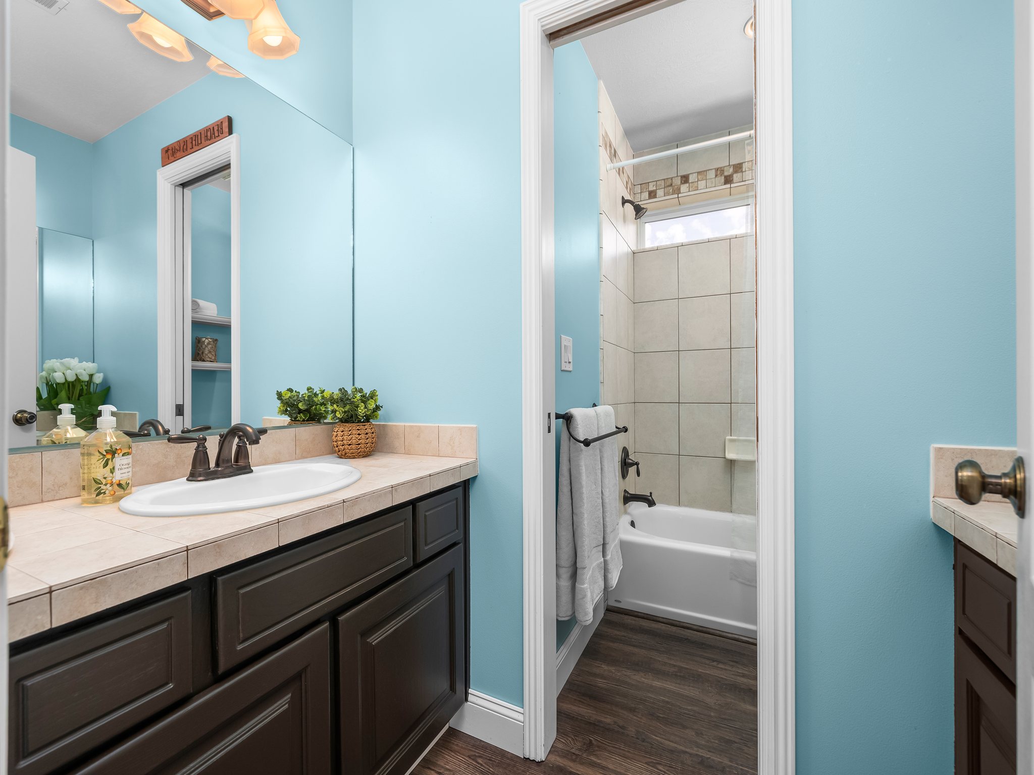 Bathroom featuring a dark wood-finish vanity with an integrated basin sink, tiled countertop, and bronze-finish hardware