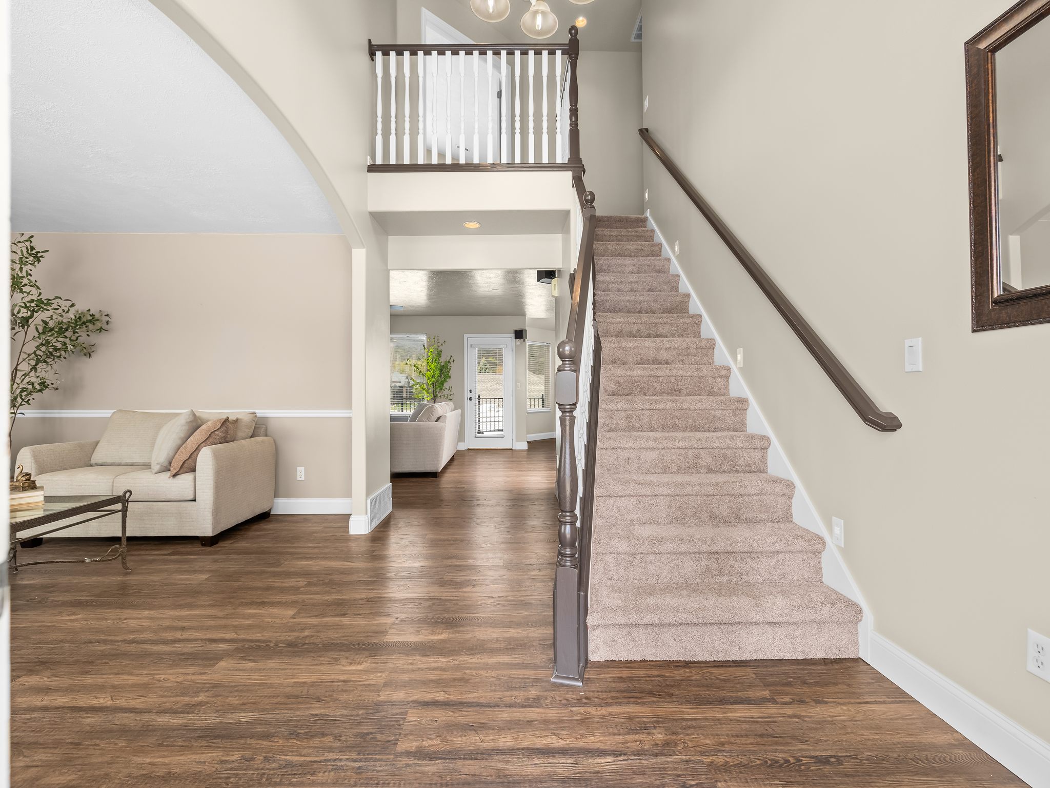Grand entryway featuring a carpeted staircase with a dark wood handrail and white balusters, wood-finish flooring, and light-toned walls with wainscoting