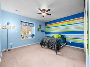 Carpeted room featuring a window with blinds, ceiling fan with integrated lighting, a colorful accent wall, and built-in shelving