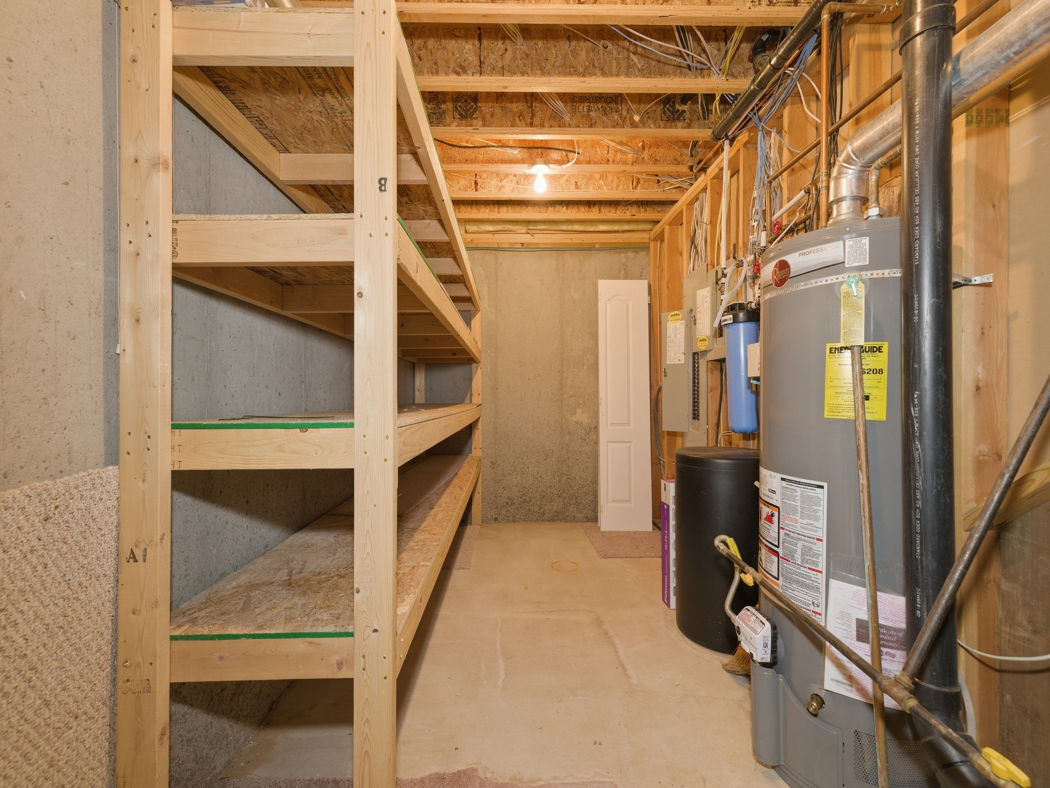 Lower level utility area featuring built-in wood shelving, exposed ceiling joists, concrete flooring, and a water heater