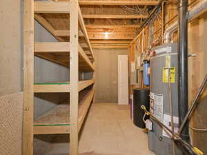 Lower level utility area featuring built-in wood shelving, exposed ceiling joists, concrete flooring, and a water heater