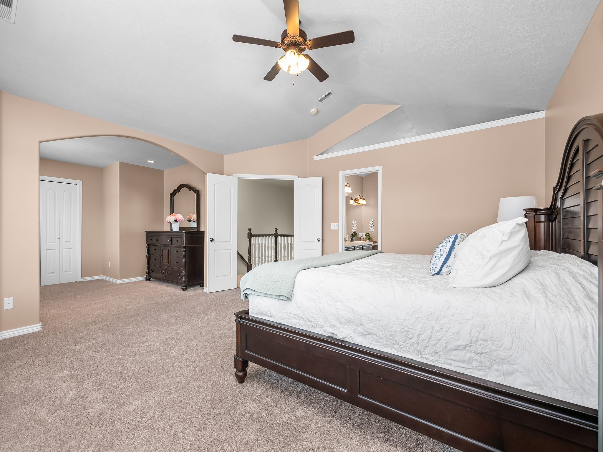 Carpeted bedroom featuring an arched doorway, bi-fold closet doors, a ceiling fan with integrated lighting, and vaulted ceilings
