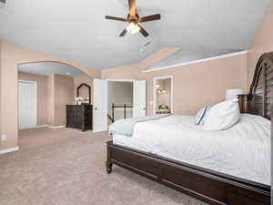 Carpeted bedroom featuring an arched doorway, bi-fold closet doors, a ceiling fan with integrated lighting, and vaulted ceilings