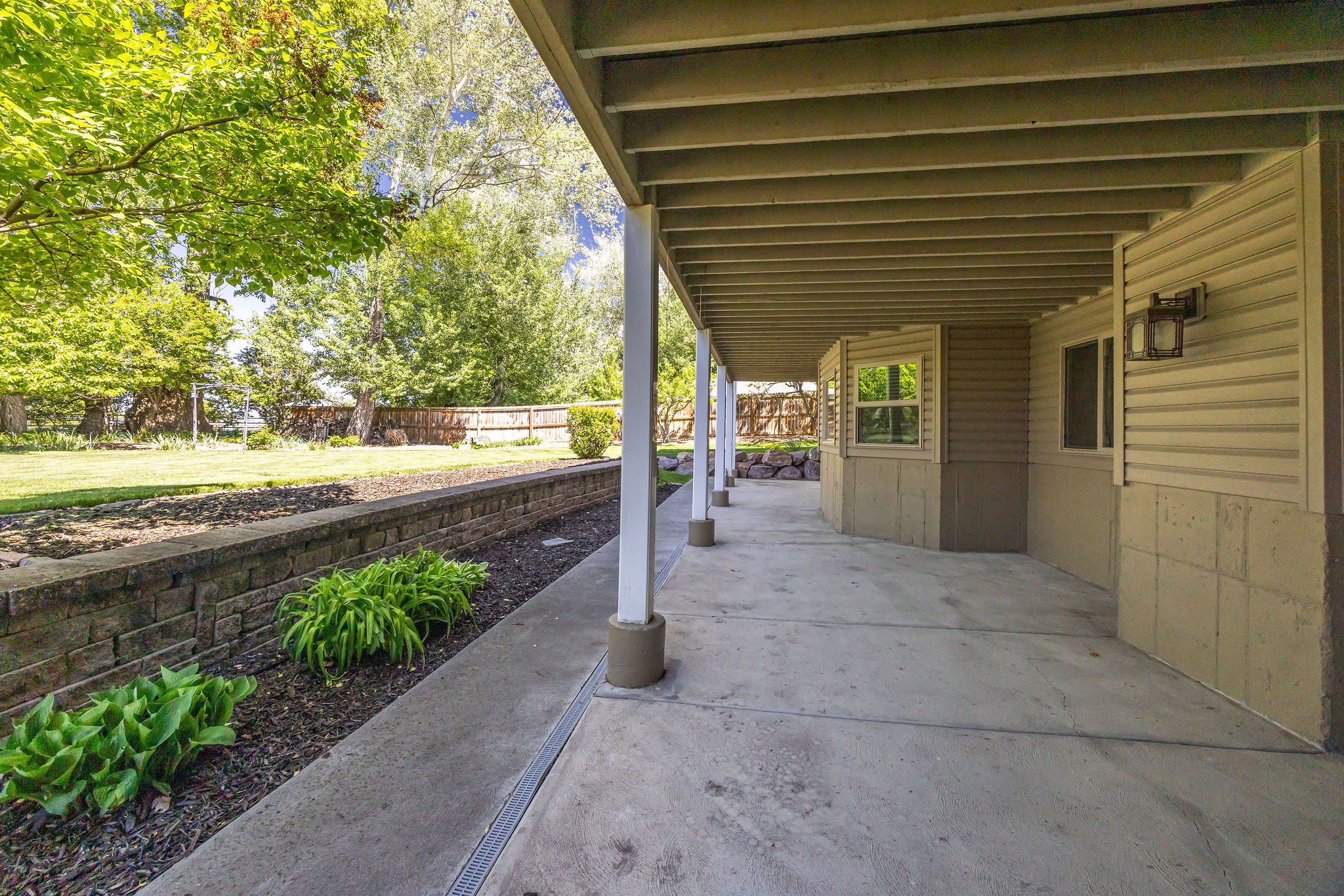 Expansive concrete patio with a covered ceiling, supported by white columns, offering an outdoor extension of the home