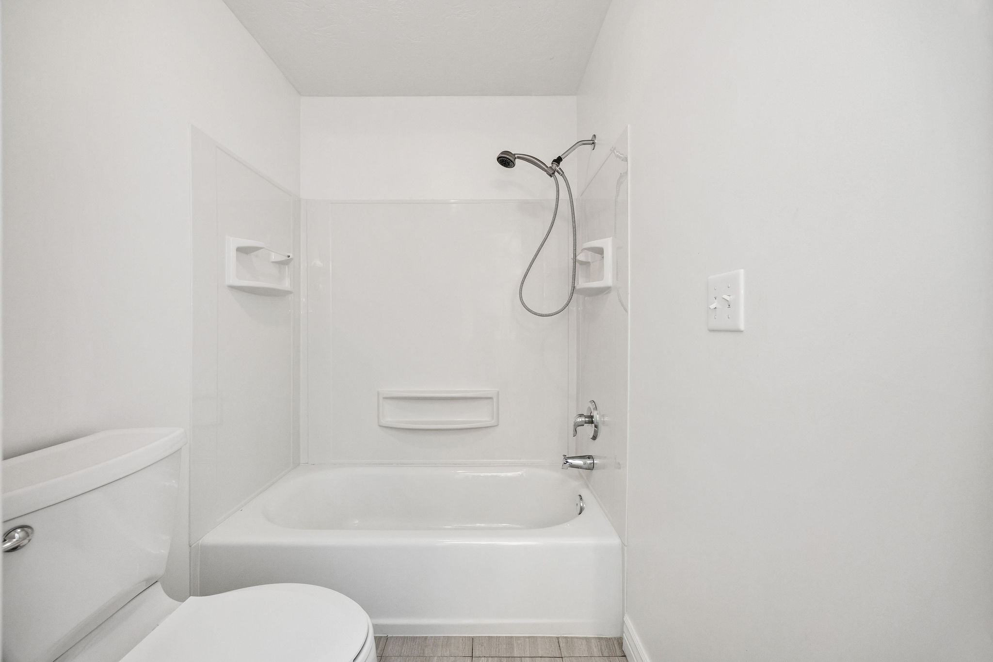 White bathtub with integrated shower, chrome fixtures, and a white tile-look surround