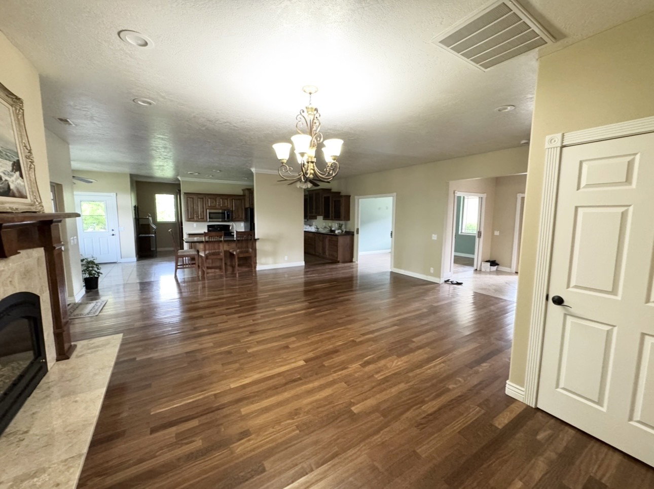 Expansive living area featuring wood-finish flooring, a decorative fireplace with a stone surround, recessed ceiling lighting, and a chandelier