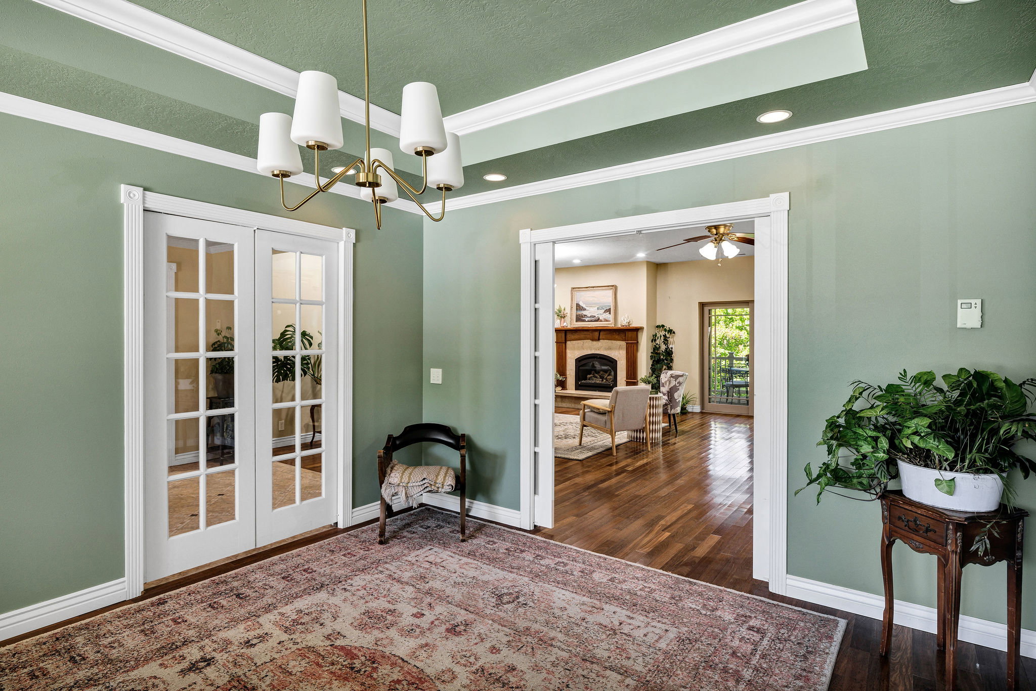Room featuring a tray ceiling with recessed lighting and a brass chandelier, a wide entryway, and white French doors