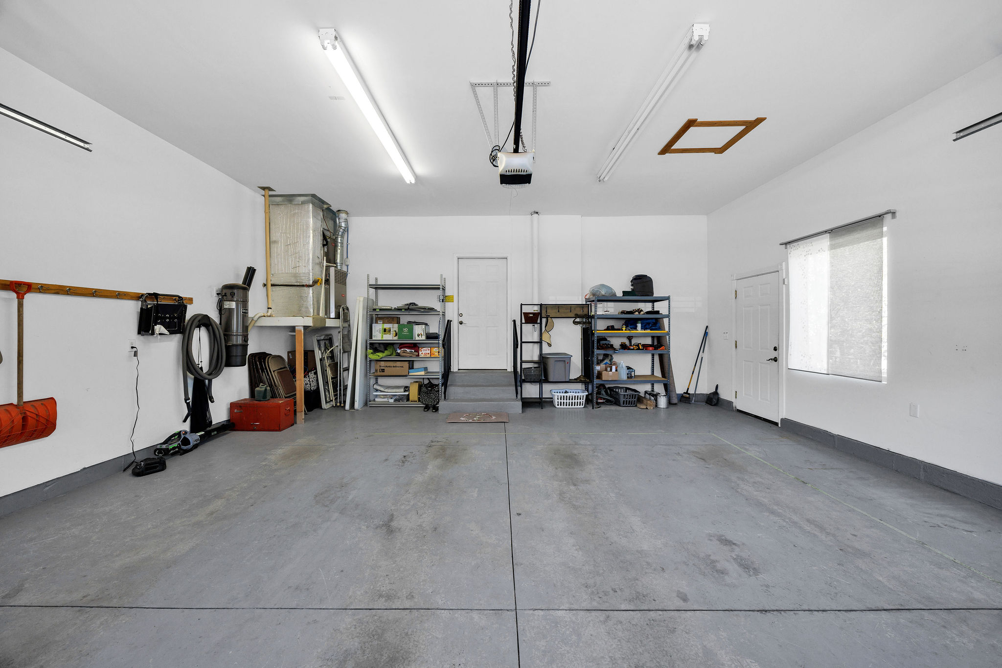 Spacious garage featuring concrete flooring, multiple fluorescent lighting fixtures, and a garage door opener